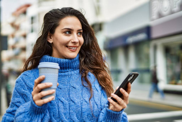 Young hispanic woman using smartphone drinking coffee at the city. - Фото, зображення