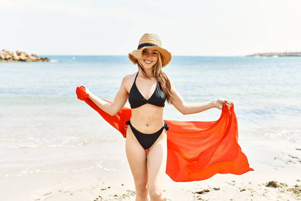 Νεαρή Κουακασιάτισσα χαμογελαστή χαρούμενη φορώντας μπικίνι στην παραλία. - Φωτογραφία, εικόνα