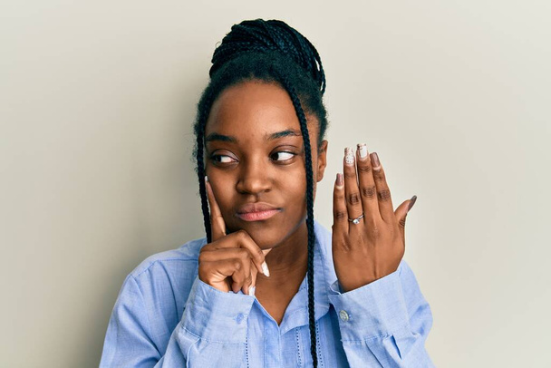 Mulher afro-americana com cabelo trançado vestindo anel de noivado rosto sério pensando em questão com a mão no queixo, pensativo sobre ideia confusa  - Foto, Imagem