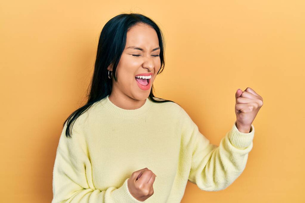 Beautiful hispanic woman with nose piercing wearing casual yellow sweater celebrating surprised and amazed for success with arms raised and eyes closed  - Photo, Image