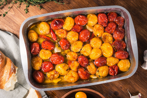 Homemade confit of colorful tomatoes with garlic, hot pepper and thyme with olive oil on a baking sheet, close-up, top view - Foto, Imagem