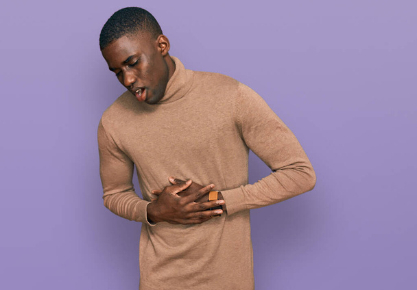 Молодий афроамериканець у звичайному зимовому светрі з руками на живіт, тому що нудота, болюча хвороба, почувається недобре. божевілля.  - Фото, зображення