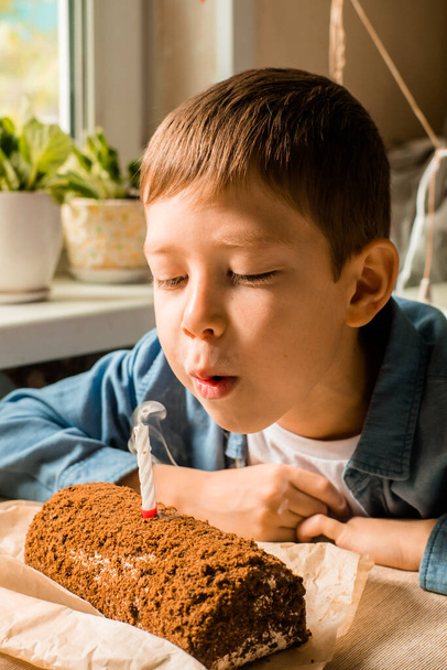 boy of 9 years old blows out the candle on the cake. celebrating birthday at home. Home holiday for children. portrait of a boy blowing on a candle. Make a wish. Fulfillment of desires - Photo, image