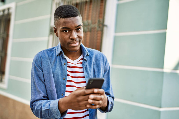 Молодой африканский американец улыбается счастливо, используя смартфон в городе. - Фото, изображение
