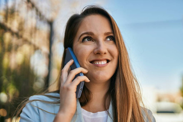 Jovem mulher de negócios loira sorrindo feliz falando no smartphone na cidade. - Foto, Imagem