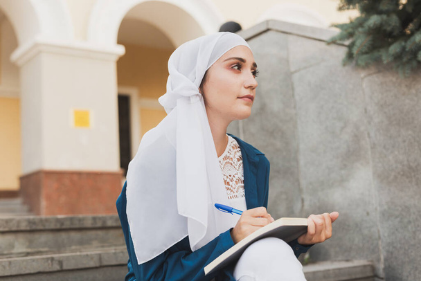 Studentka z Bliskiego Wschodu siedzi na schodach w kampusie uniwersyteckim. Koncepcja edukacji i wiedzy. - Zdjęcie, obraz