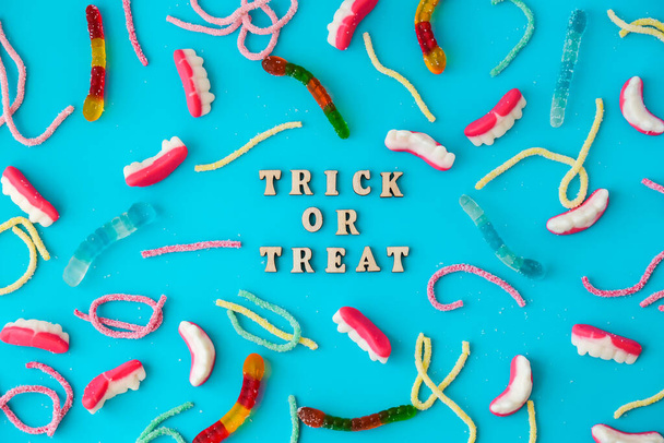 Halloween concept. Halloween party decorations with words TRICK OR TREAT, sweets, top view flat lay on blue background. Greeting card - Zdjęcie, obraz