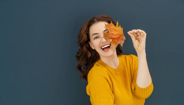 Happy emotional young woman laughing with yellow leaf on dark wall background. - Foto, Bild