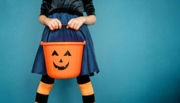 Happy Halloween! Cute little lgirl with pumpkin basket on blue wall background.  - Photo, Image