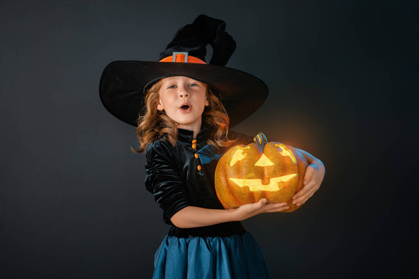 Happy Halloween! Cute little laughing girl in witch costume on black wall background.  - Foto, Bild