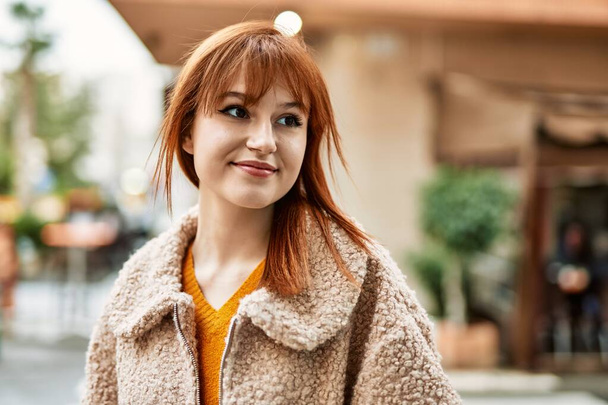 Young redhead girl smiling happy standing at the city. - Φωτογραφία, εικόνα