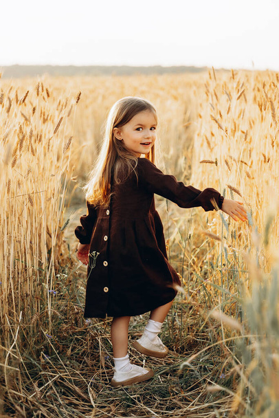 Little beautiful smiling girl on a gold wheat field. Girls in the grain-field. Cute little girl in the summer field of wheat.  - Valokuva, kuva