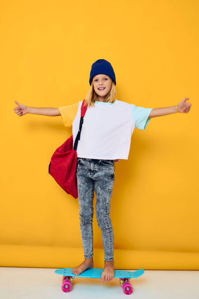 stylish girl rides a skateboard with a red backpack yellow background - Zdjęcie, obraz