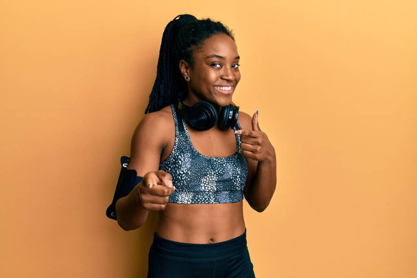 Africká Američanka s copánkovými vlasy na sobě sportovní oblečení a páskou ukazující prsty na kameru se šťastnou a zábavnou tváří. dobrá energie a vibrace.  - Fotografie, Obrázek