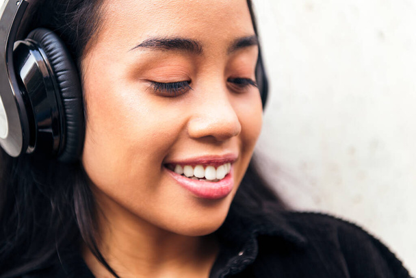 portrait of a cheerful young asian woman with headphones enjoying listening to music outdoors - Fotografie, Obrázek