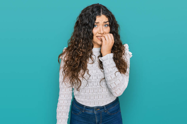 Jong Latijns-Amerikaans meisje draagt casual kleding die er gestrest en nerveus uitziet met handen op de mond bijtende nagels. angstprobleem.  - Foto, afbeelding