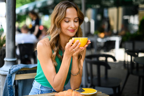 Smiling woman having breakfast outdoor in a city - Fotó, kép