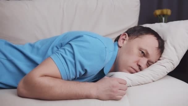 Man valt op een gezellige lichte bank en valt in slaap, concept van ontspanning na een harde dag - Video