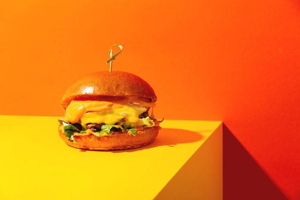 Parlak turuncu ve sarı arka planda peynirli büyük hamburger. Modern tarzda Amerikan Fast Food mutfağı.. - Fotoğraf, Görsel