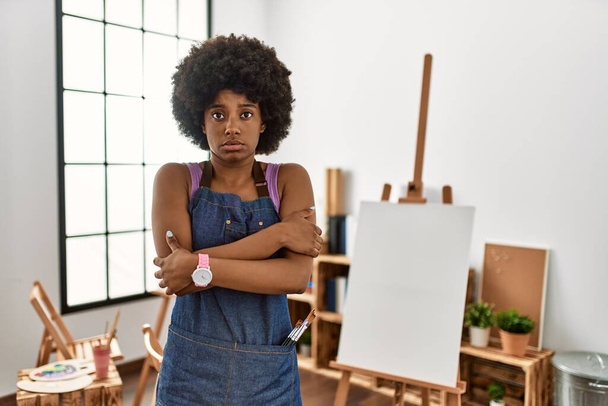 Mladá africká americká žena s afro vlasy v uměleckém studiu třepání a mrazení pro zimní chlad se smutným a šokujícím výrazem na tváři  - Fotografie, Obrázek