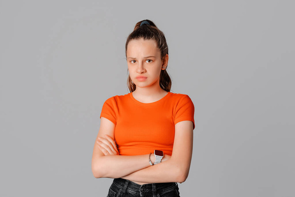 Angry brunette teen girl feel unfair and displeased, cross arms on chest and frowning, condemn something bad or upsetting, standing on gray background. Young emotional woman - Photo, Image