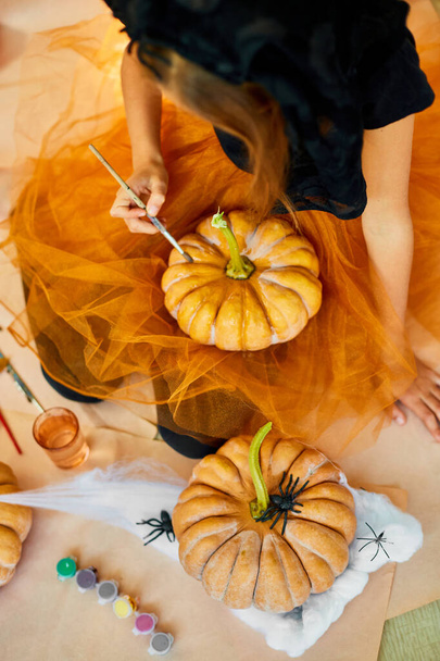 Gros plan méconnaissable de la main d'une jeune fille décorant une citrouille orange, dessinant le visage Jack-O-Lantern pour Halloween avec une peinture à la maison. Concept de décoration de vacances - Photo, image