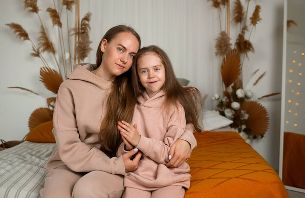 portret pięknej matki i córeczki w identycznych garniturach siedzącej na łóżku - Zdjęcie, obraz