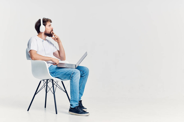 hombre de camiseta blanca sentado en una silla con un portátil en auriculares. Foto de alta calidad - Foto, Imagen