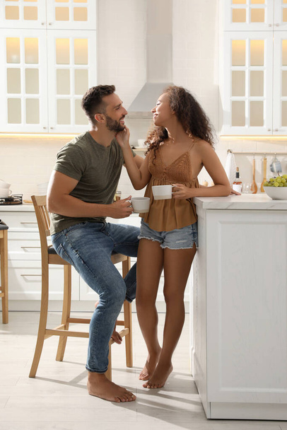 Lovely couple with cups of drink enjoying time together in kitchen at home - Foto, Bild