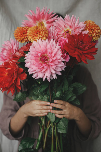 Φθινόπωρο λουλούδια μπουκέτο σε γυναικεία χέρια κοντά στο ρουστίκ δωμάτιο. Γυναίκα σε λινό φόρεμα κρατώντας όμορφα πολύχρωμα ντάλιες. Φθινοπωρινή περίοδος στην ύπαιθρο, αγροτική αργή ζωή. Αισθητική - Φωτογραφία, εικόνα