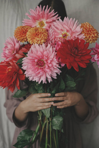 Autumn flowers bouquet in woman hands close up in rustic room. Woman in linen dress holding beautiful colorful dahlias. Autumn season in countryside, rural slow life. Aesthetic - 写真・画像