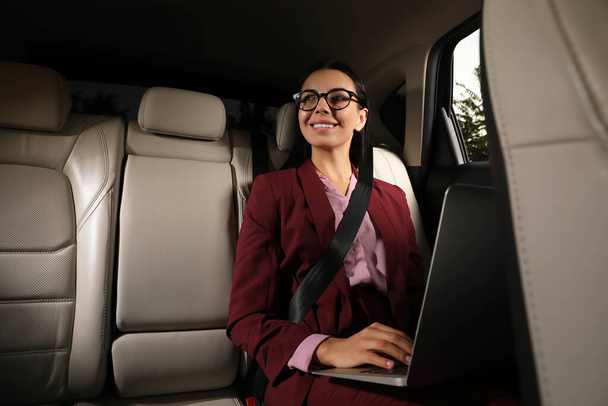Young woman working on laptop in modern taxi, space for text - Foto, imagen