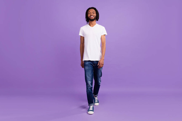 Full length photo of charming dark skin young man walk smile good mood weekend isolated on violet color background - Fotoğraf, Görsel