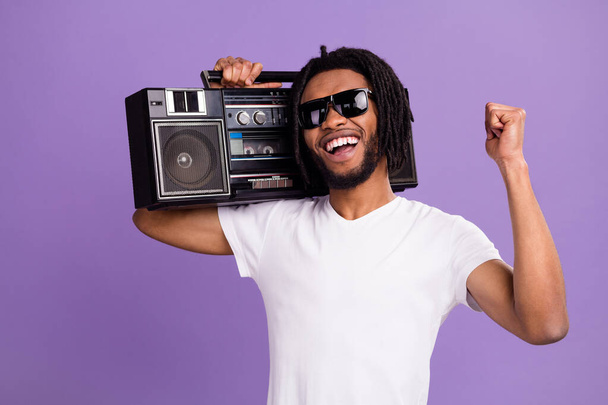 Portrait of attractive cheerful guy carrying tape player having fun rest isolated over bright violet purple color background - Фото, зображення