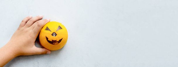 De handen van een jongen die een enge muilkorf op een pompoen tekent voor de feestdag van Halloween. Minimalisme. Grijs en oranje. - Foto, afbeelding