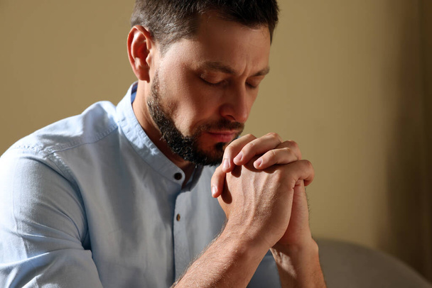 Religious man with clasped hands praying indoors - Foto, afbeelding