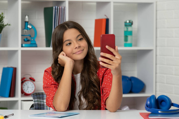 šťastný dítě dlouhé kudrnaté vlasy s selfie foto na smartphonu ve třídě, vlogging - Fotografie, Obrázek