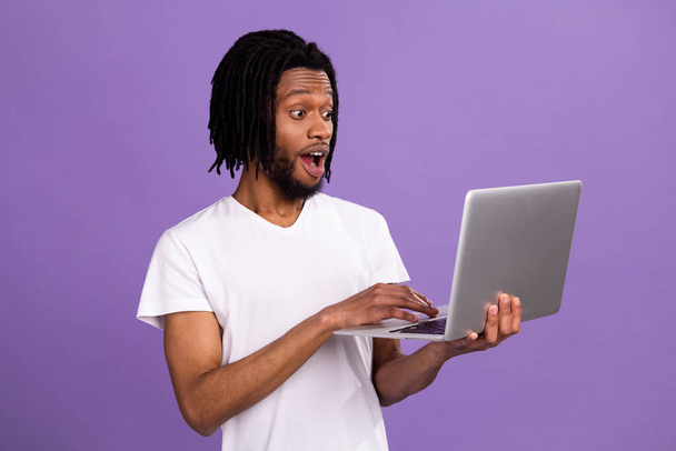 Портрет привлекательный изумленный веселый парень печатает с помощью ноутбука изолированы на ярко-фиолетовый фиолетовый цвет фона - Фото, изображение