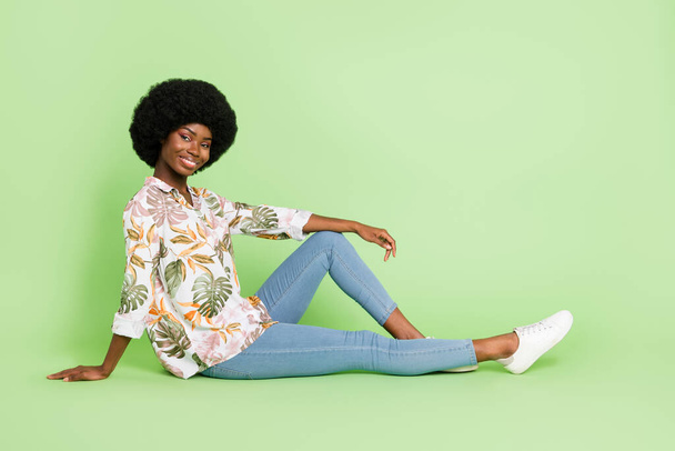 Full body profil boczny zdjęcie młodej czarnej dziewczyny szczęśliwy pozytywny uśmiech siedzieć podłogi casual strój izolowany nad zielonym tle kolor - Zdjęcie, obraz