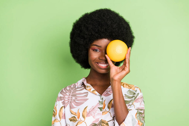 Photo of young attractive african girl happy positive smile cover eye orange fruit isolated over green color background - Valokuva, kuva