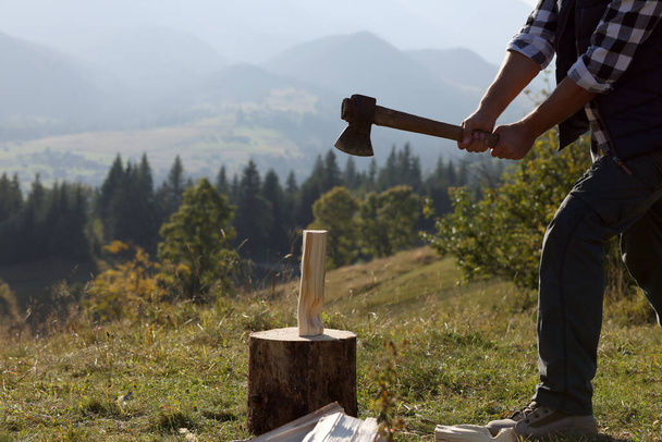 Man with axe cutting firewood on hill, closeup - Фото, изображение
