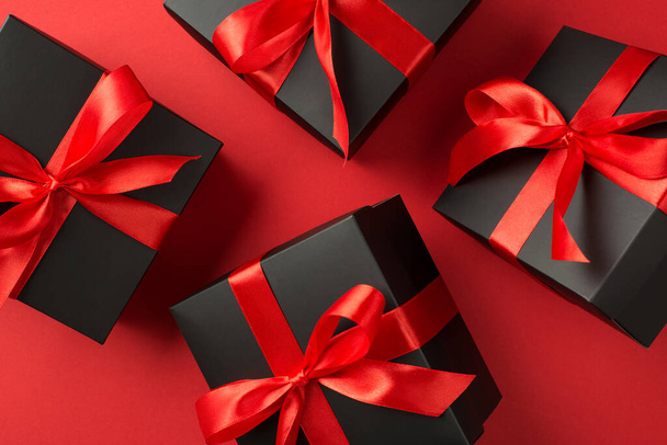 Вид зверху фото вирівнюючих чорних подарункових коробок з бантом червоної стрічки на ізольованому червоному тлі
 - Фото, зображення