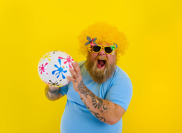 Товстий чоловік з перукою в голові і сонцезахисні окуляри розважаються з м'ячем
 - Фото, зображення