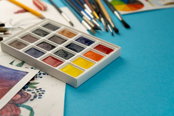 A box of watercolors with brushes. Draw, background. Packing of multicolored new paints on the table. Brush and paint. Drawing and hobbie. - Photo, image