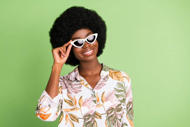 Photo of positive traveler girl beaming smile posing wear sunglass floral print shirt isolated on green color background - Photo, Image