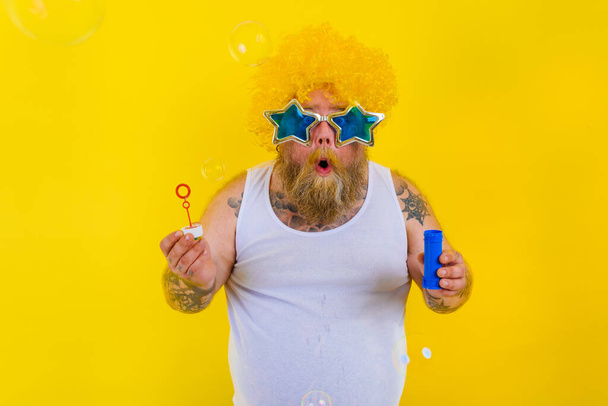 Hombre sorprendido con peluca amarilla en la cabeza jugar con jabón de burbujas - Foto, imagen