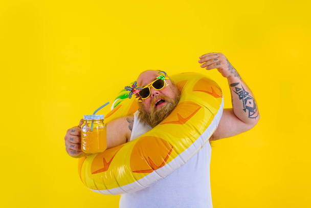 Gordo irritado homem com peruca na cabeça está pronto para nadar com um salva-vidas donut - Foto, Imagem