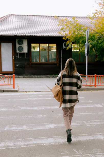 красивая девушка в модной осенней одежде с рюкзаком во время перехода через дорогу в городе - Фото, изображение