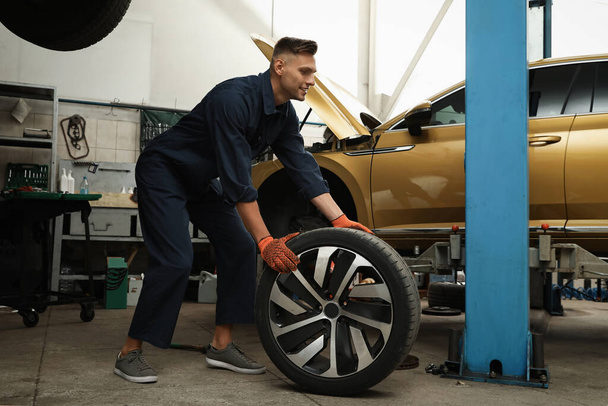 Professional mechanic with car wheel at automobile repair shop - Φωτογραφία, εικόνα
