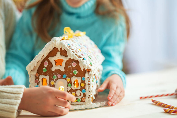 Close-up, children hold a handmade Christmas gingerbread house decorated with sweets in the shape of a star. Delicious cookies prepared for the holiday. - Fotoğraf, Görsel